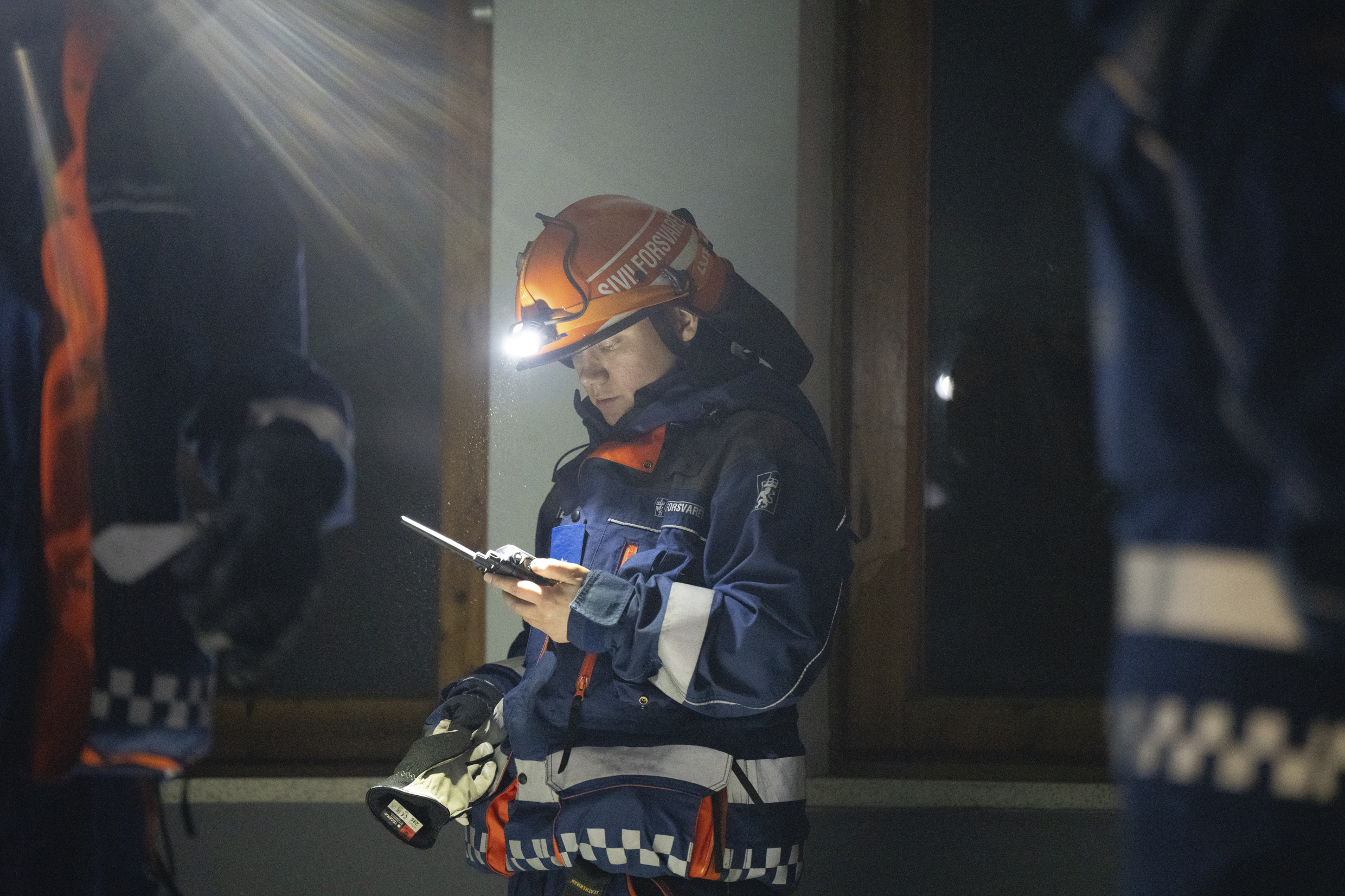 Person i Sivilforsvarsuniform med hodelykt i mørkt rom
