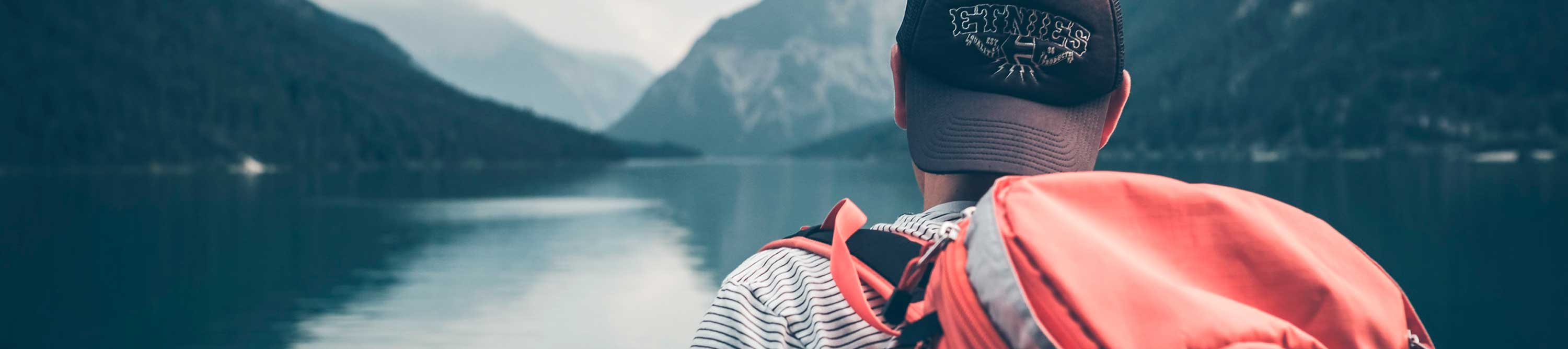 Person med sort caps og ryggsekk ser ut over fjord mellom høye fjell